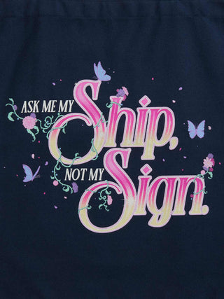 A close-up of a dark navy blue garment featuring a colorful graphic print with the text 'ASK ME MY Ship, NOT MY Sign' in pink, purple, and cream lettering, decorated with butterflies and floral vines.