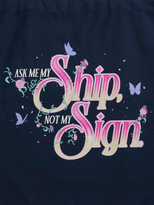 A close-up of a dark navy blue garment featuring a colorful graphic print with the text 'ASK ME MY Ship, NOT MY Sign' in pink, purple, and cream lettering, decorated with butterflies and floral vines.