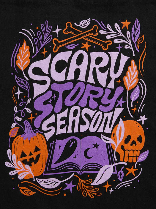 A Halloween-themed graphic print featuring the text 'SCARY STORY SEASON' in stylized purple and white lettering, surrounded by orange pumpkins, a skull, an open book, bones, leaves, and stars on a black background.