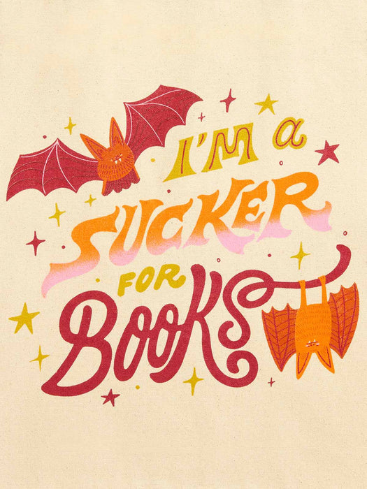 A retro-style typographic illustration on a warm cream background featuring the phrase “I’m a sucker for books” in red, orange, and yellow lettering, with bat illustrations and small star accents.