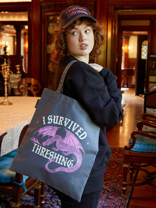 Person holding a tote bag with a dragon design and text in an elegant room.