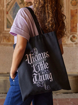Person carrying a black tote bag with decorative text in an indoor setting