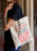 Person holding a tote bag with a red and black text design.