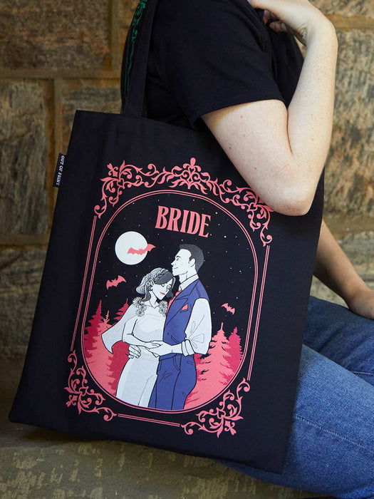 Person holding a tote bag with a 'Bride' design featuring a couple and moon.