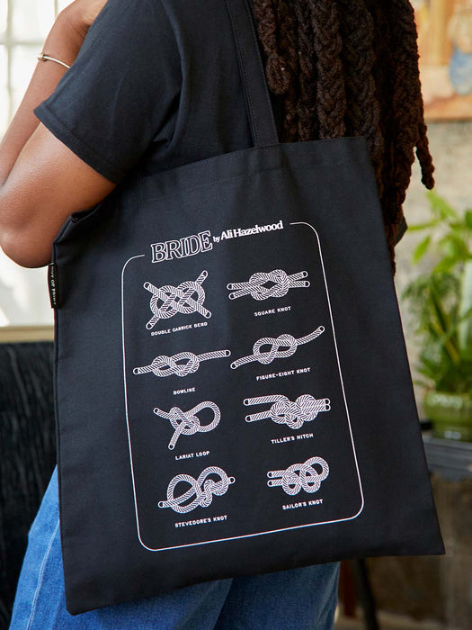 Black tote bag with white knot designs and 'BRIDE' text held by a person.