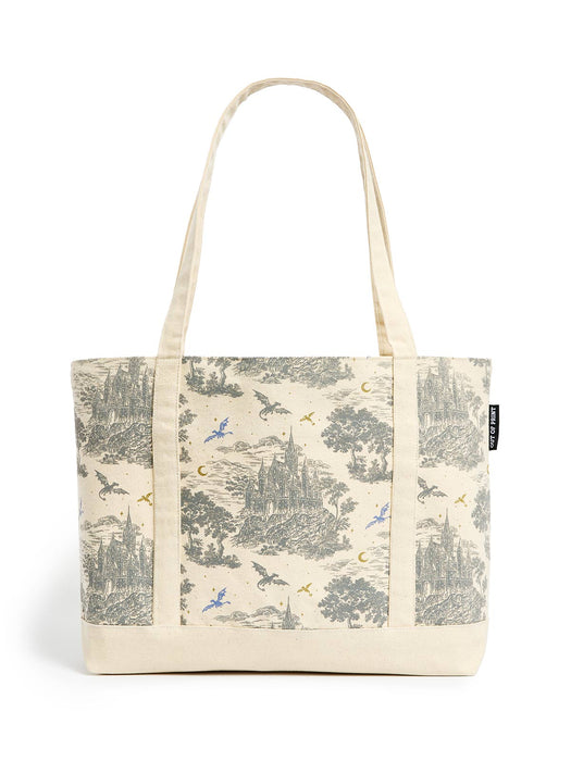 A canvas tote bag with a cream-colored base and a detailed toile-style print featuring castles, trees, and flying dragons in muted gray, blue, and gold tones. The bag has two long cream handles and a small black brand tag on the right side.