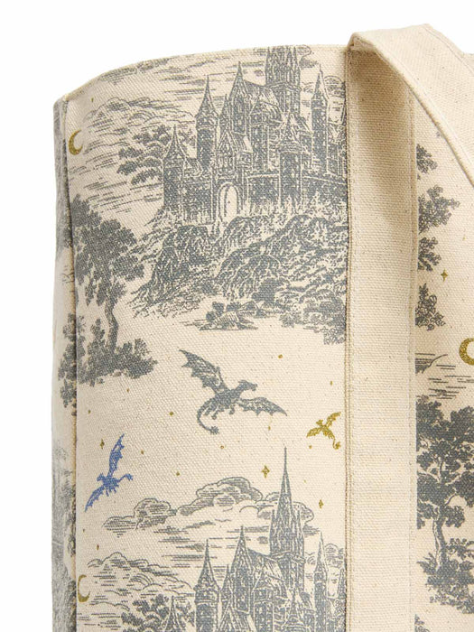 Close-up of a canvas tote bag featuring a detailed black and blue castle and dragon toile de jouy pattern on a cream background.