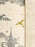 Close-up of a woven textile with an off-white background, featuring a gray printed topper-style illustration of a spire, clouds, and a dragon, plus small metallic gold star and dragon accents. A vertical stitched seam runs along the right side.