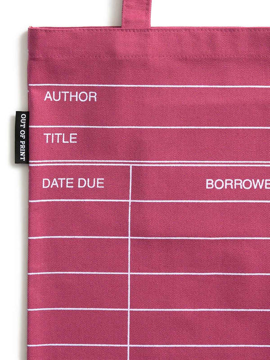 A close-up of a maroon red canvas tote bag with white printed lines and text fields for borrowing information: AUTHOR, TITLE, DATE DUE, and BORROWER. A small black fabric tag on the left reads OUT OF PRINT.