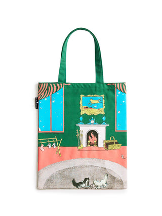 A green fabric tote bag featuring a whimsical illustrated scene of a woman sitting by a fireplace with cats at the bottom, set against a plain white background.