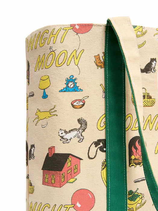 A close-up of a canvas tote bag with a beige background printed with whimsical cartoon illustrations and yellow text, featuring a prominent dark green fabric strap.