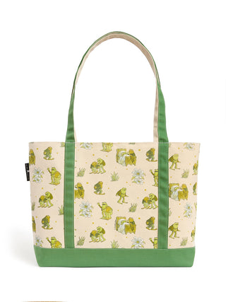 A canvas tote bag featuring a cream background printed with green frogs, white flowers, and small yellow stars, accented with solid green handles and bottom trim.