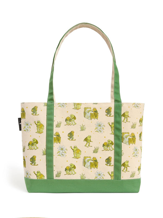A canvas tote bag featuring a cream background printed with green frogs, white flowers, and small yellow stars, accented with solid green handles and bottom trim.