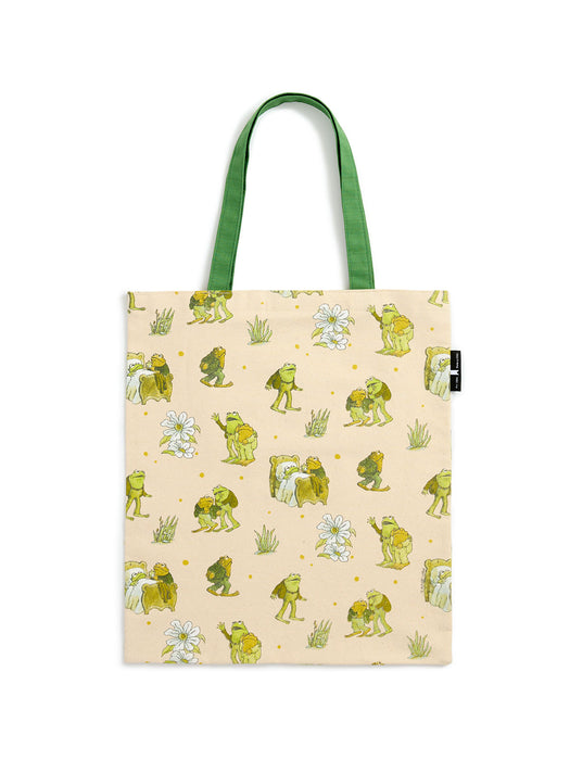 A canvas tote bag with a light beige background printed with a pattern of green frogs, white flowers, and small yellow dots, featuring green shoulder straps.