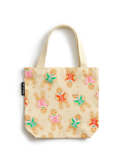 A cream canvas mini tote bag featuring an all-over print of gingerbread cookies reading books, with two top handles and a small black brand tag on the side.