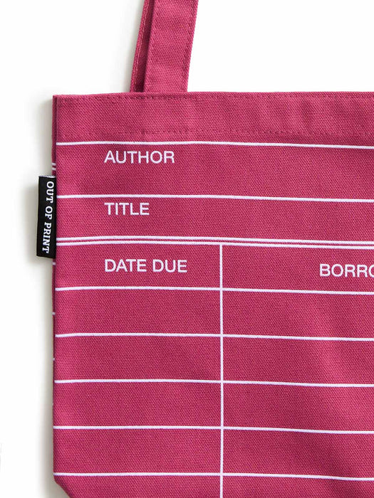 A close-up of a maroon red canvas tote bag with white horizontal lines and printed text fields for author, title, date due, and borrower. A black fabric tag on the left reads OUT OF PRINT.