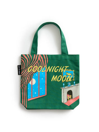 A green canvas tote bag with a colorful 'Goodnight Moon' illustration, featuring a window with a moon view, wavy curtains, and a cozy fireplace scene, set against a plain white background.
