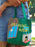 A green canvas mini tote bag with a colorful graphic print of a window showing a full moon and the words 'GOODNIGHT MOON!' in yellow, carried by a person wearing denim shorts outdoors.