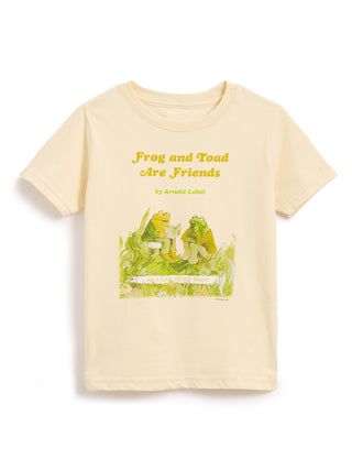 A cream-colored short-sleeve t-shirt featuring a graphic print of the 'Frog and Toad Are Friends' book cover, including the title in yellow text and the illustration below, displayed on a clean white background.