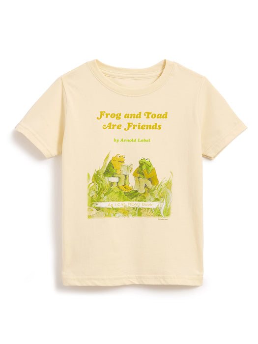 A cream-colored short-sleeve t-shirt featuring a graphic print of the 'Frog and Toad Are Friends' book cover, including the title in yellow text and the illustration below, displayed on a clean white background.
