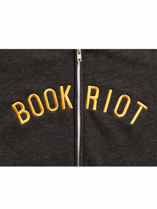 Close-up of a dark charcoal zip-up hoodie with 'BOOK RIOT' embroidered in yellow across the chest, centered on a white background.
